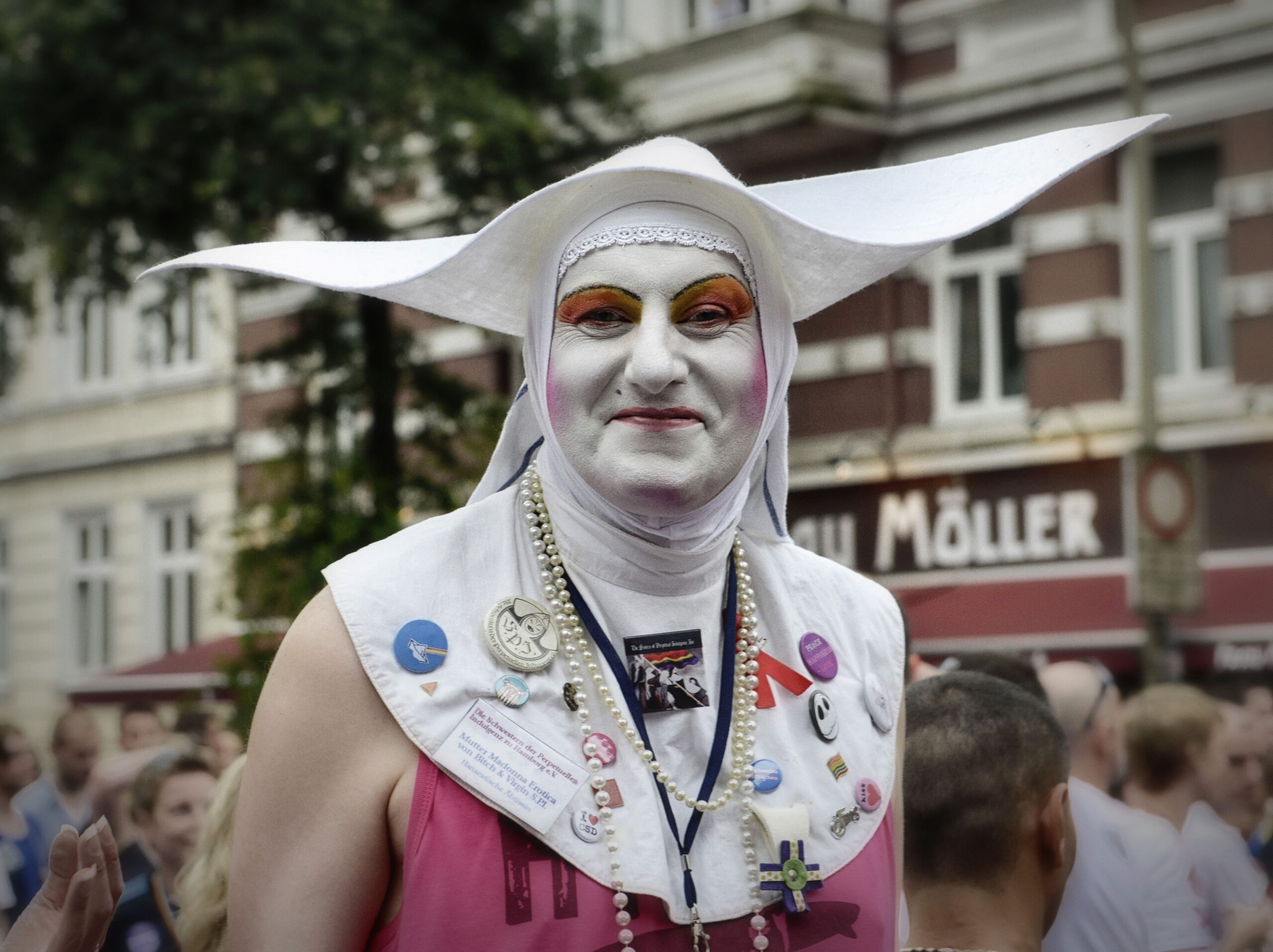 Die Äbtissin des Hamburger Hauses beim CSD mit großer weißer Flügelhaube, weißem Gesichtsmake-up, pinkfarbener Kleidung und zahlreichen Ansteckern und Perlenketten.